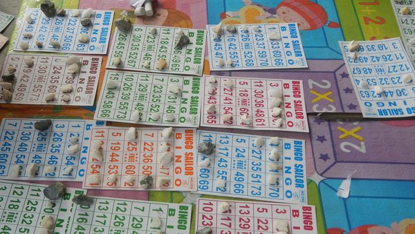 Many paper bingo cards laid out on a table, numbers covered with small markers during a game