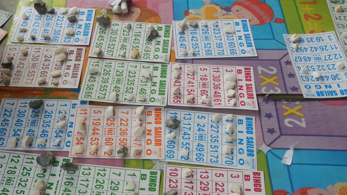 Many paper bingo cards laid out on a table, numbers covered with small markers during a game