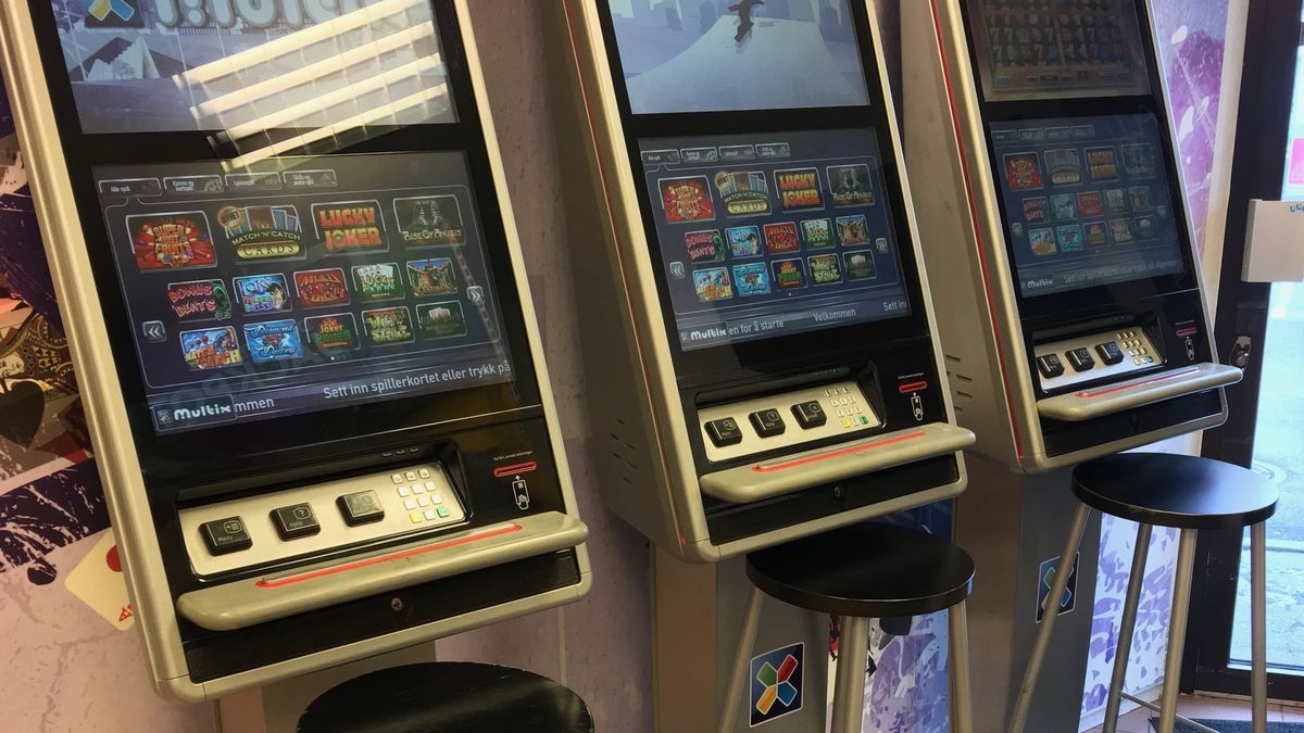 Three video lottery terminals in a row, touch screens showing game menus, with empty bar stools in front